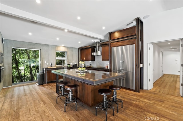 kitchen featuring light hardwood / wood-style floors, stainless steel built in fridge, oven, a kitchen island, and a breakfast bar