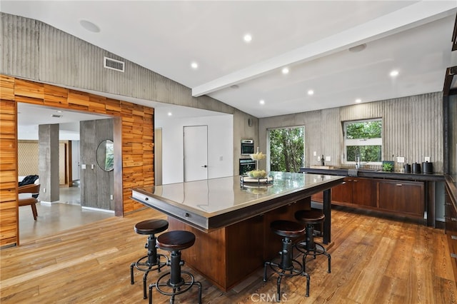 kitchen with wood walls, light hardwood / wood-style floors, beamed ceiling, a breakfast bar area, and a large island