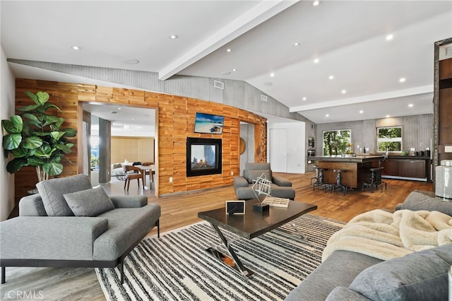 living room with a multi sided fireplace, light hardwood / wood-style floors, wood walls, and lofted ceiling with beams