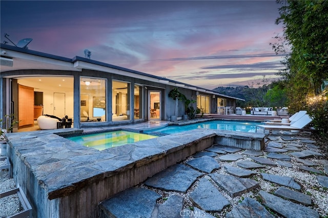 pool at dusk with a patio area and an in ground hot tub