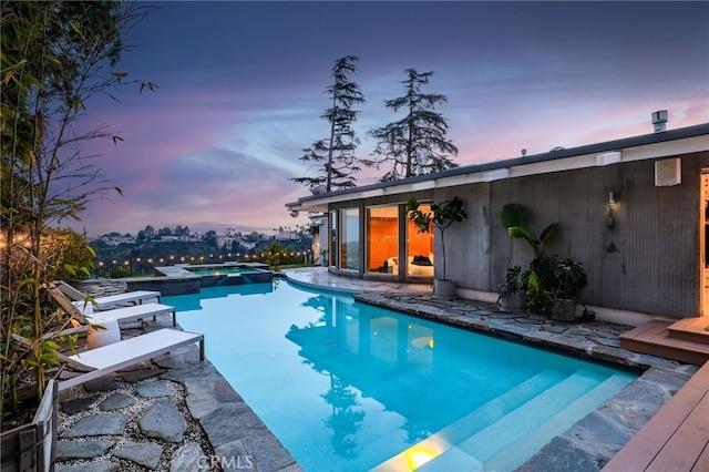 pool at dusk featuring an in ground hot tub