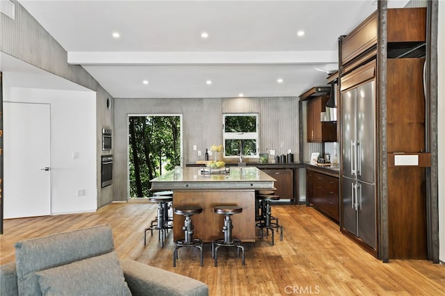 kitchen featuring a kitchen island, a breakfast bar, beamed ceiling, light hardwood / wood-style flooring, and stainless steel appliances