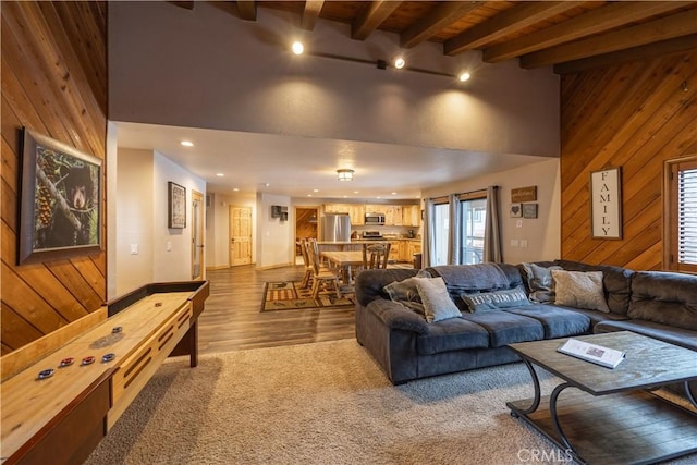 living room with light colored carpet, a wealth of natural light, beamed ceiling, and wooden walls