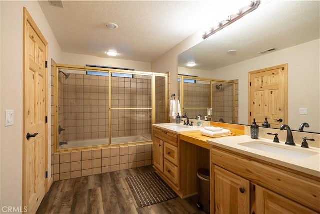 bathroom with a textured ceiling, enclosed tub / shower combo, wood-type flooring, and vanity