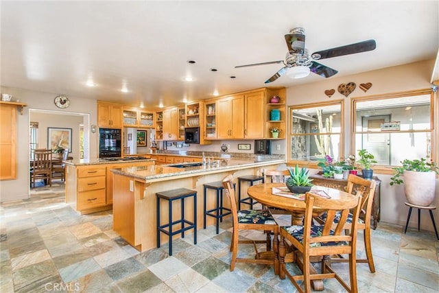 kitchen featuring glass insert cabinets, light stone counters, a peninsula, black appliances, and a kitchen bar