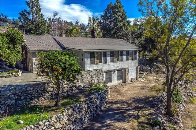 view of home's exterior with stone siding, a shingled roof, and a chimney