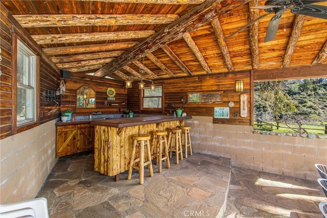 bar with ceiling fan, bar, wood ceiling, vaulted ceiling, and stone finish floor