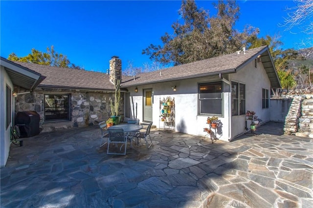 back of property with a shingled roof, a chimney, outdoor dining area, a patio area, and stucco siding