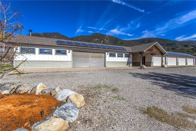 view of front facade featuring solar panels, an attached garage, board and batten siding, a mountain view, and driveway