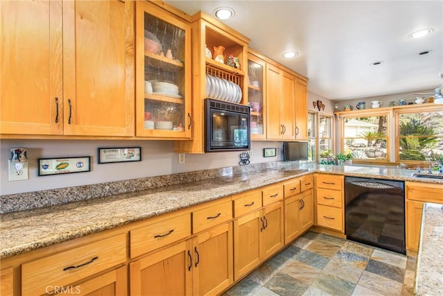 kitchen featuring light stone countertops, black appliances, glass insert cabinets, and a sink