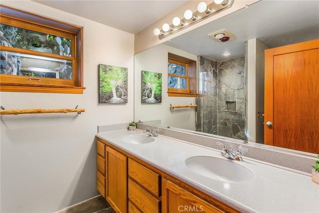 full bath with a sink, a marble finish shower, and double vanity