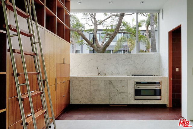 kitchen with sink, gas cooktop, dark tile patterned flooring, oven, and decorative backsplash