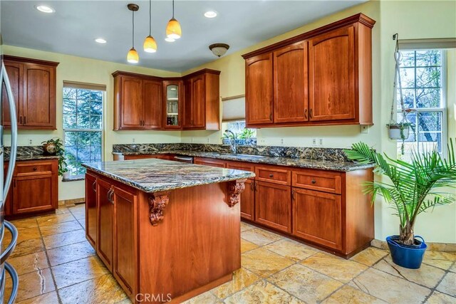 kitchen with dark stone counters, decorative light fixtures, a kitchen island, and a healthy amount of sunlight