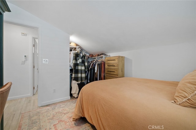 bedroom with light hardwood / wood-style flooring, vaulted ceiling, and a closet