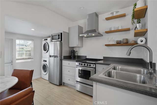 kitchen with wall chimney exhaust hood, stainless steel appliances, sink, light hardwood / wood-style flooring, and stacked washer and dryer