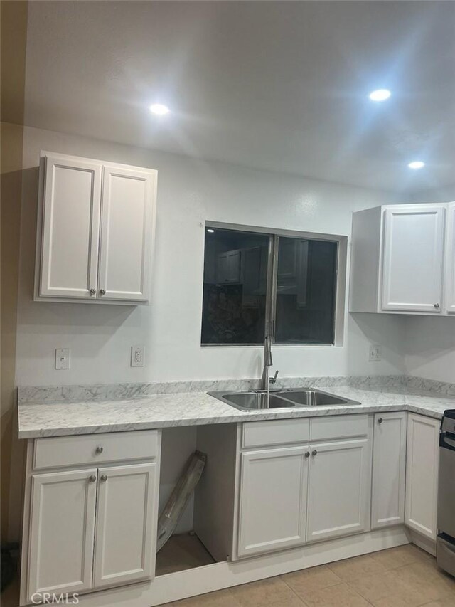 kitchen featuring white cabinetry, light tile patterned flooring, light stone countertops, range, and sink