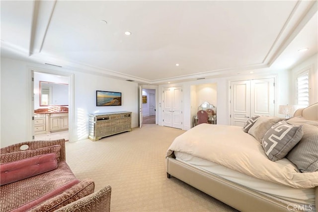 bedroom featuring a raised ceiling, light colored carpet, and connected bathroom