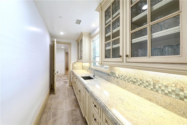 interior space featuring cream cabinets, backsplash, light stone counters, and sink