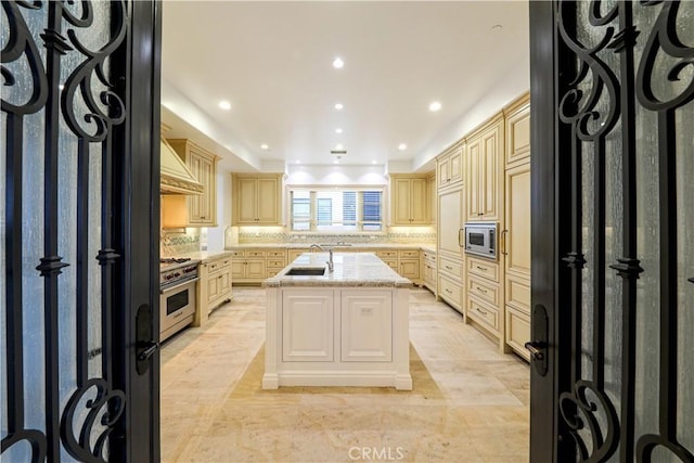 kitchen with light stone countertops, backsplash, stainless steel appliances, and a kitchen island with sink