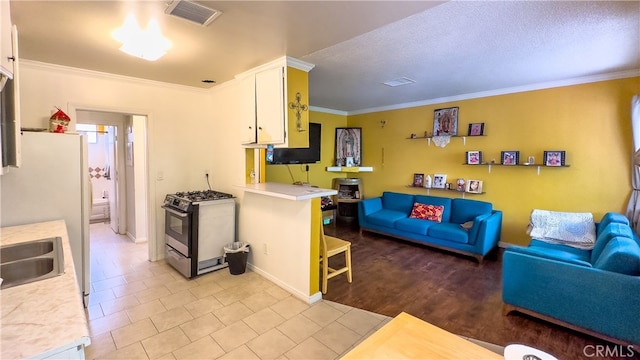 kitchen with white fridge, light tile floors, stainless steel range with gas stovetop, ornamental molding, and white cabinetry