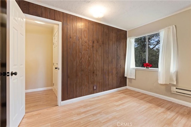 spare room with hardwood / wood-style floors, a baseboard radiator, ornamental molding, and wooden walls