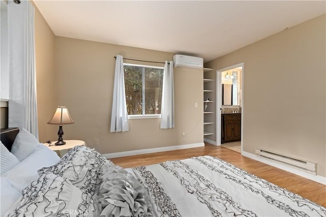 bedroom featuring ensuite bathroom, light wood-type flooring, an AC wall unit, and a baseboard heating unit