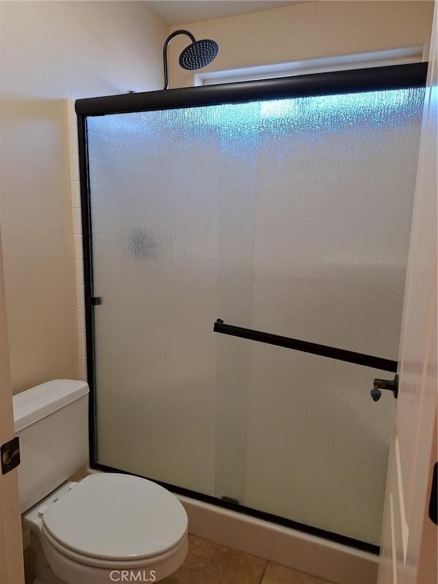 bathroom featuring a shower with shower door, tile patterned flooring, and toilet