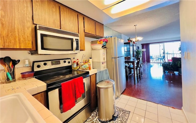 kitchen with stainless steel appliances, light tile patterned floors, pendant lighting, a chandelier, and tile counters