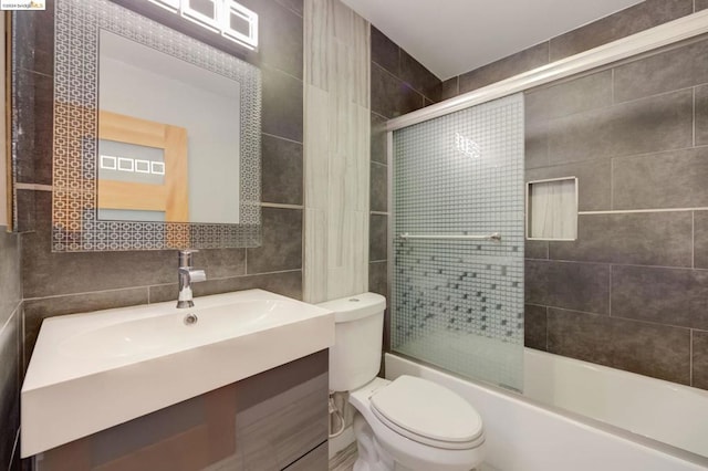 full bathroom with tile walls, toilet, oversized vanity, and bath / shower combo with glass door