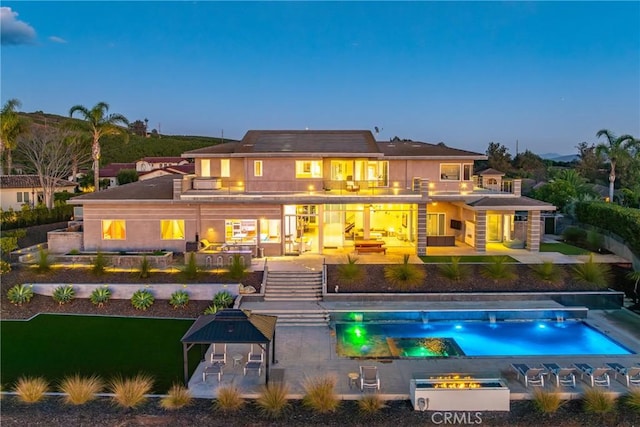 back house at dusk featuring a swimming pool with hot tub, a balcony, and a patio