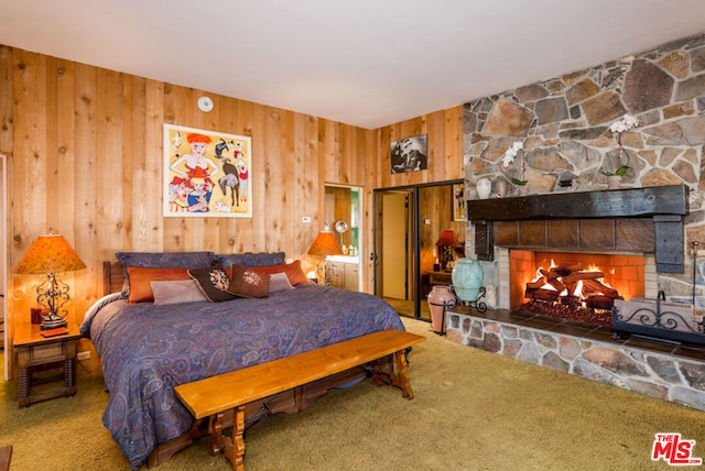 bedroom featuring a stone fireplace, wood walls, and carpet