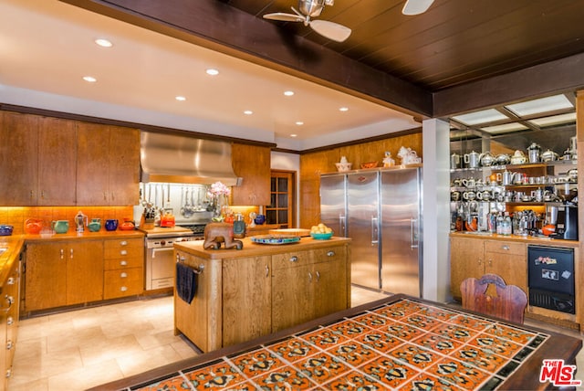 kitchen featuring ceiling fan, wall chimney exhaust hood, beamed ceiling, decorative backsplash, and appliances with stainless steel finishes