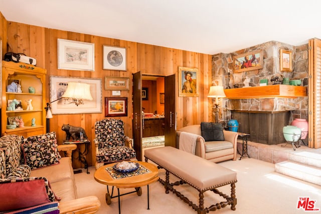 carpeted living room with a stone fireplace and wooden walls