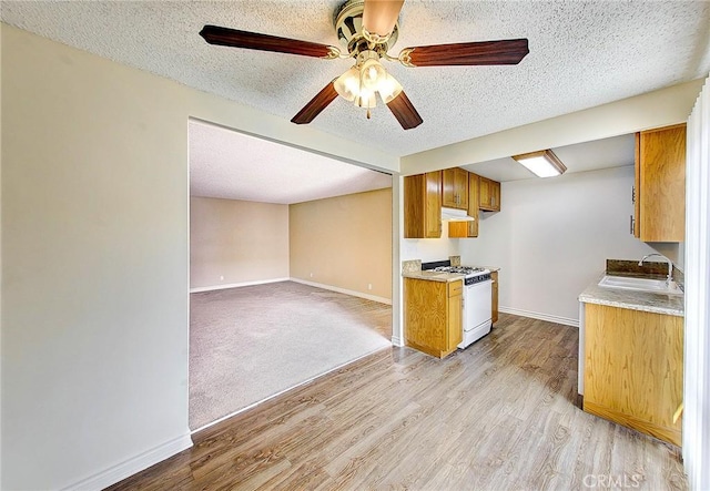 kitchen with light countertops, a sink, under cabinet range hood, and white gas range