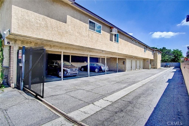 covered parking lot with a wall mounted AC, fence, and a gate