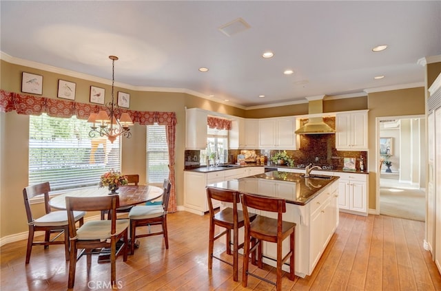 kitchen featuring pendant lighting, light hardwood / wood-style floors, white cabinetry, and an island with sink