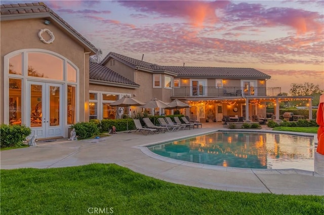 pool at dusk with a lawn, a patio, and french doors