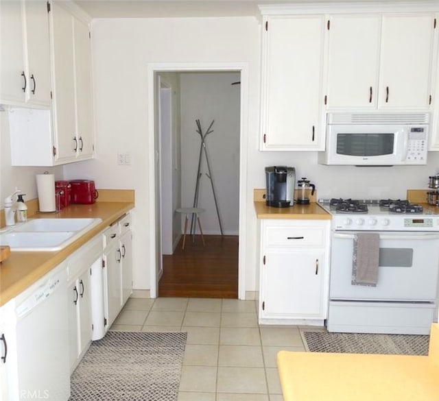 kitchen with white appliances, sink, light tile patterned floors, and white cabinets