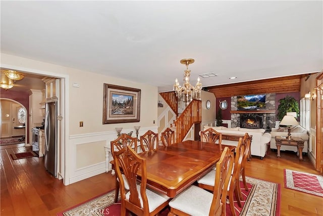 dining room featuring dark wood-type flooring, stairs, a stone fireplace, and a notable chandelier