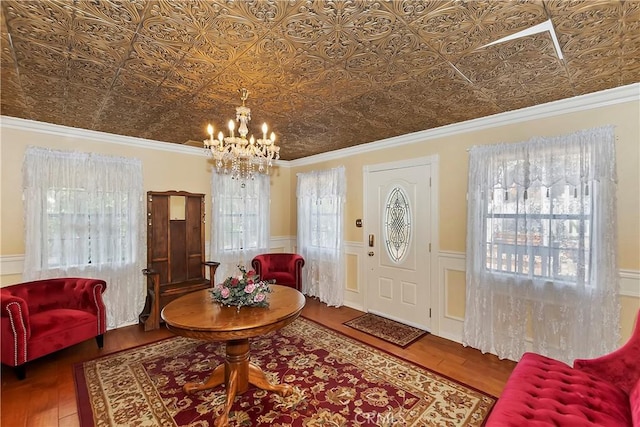 entryway with an ornate ceiling, a notable chandelier, wood finished floors, and a wainscoted wall