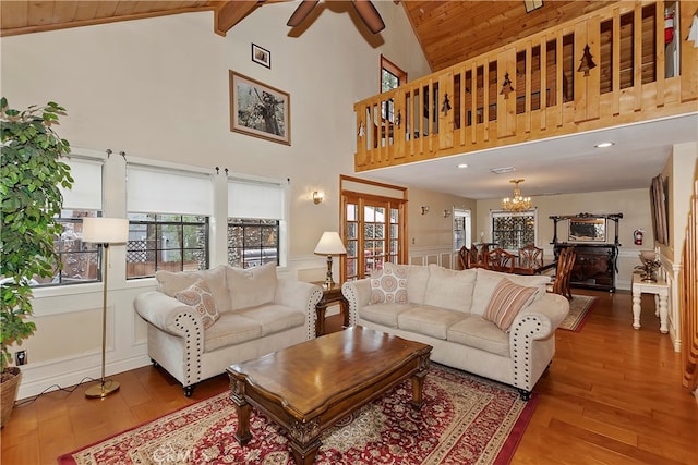 living room with wood ceiling, ceiling fan with notable chandelier, beam ceiling, high vaulted ceiling, and hardwood / wood-style floors