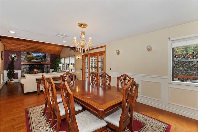 dining room with wood-type flooring, a fireplace, vaulted ceiling, and an inviting chandelier