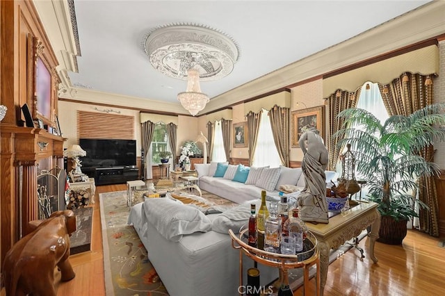 living room featuring a chandelier, ornamental molding, light hardwood / wood-style floors, and a healthy amount of sunlight