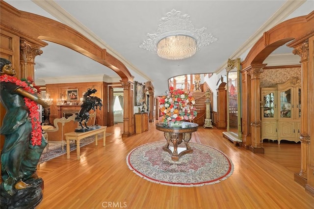 foyer with a notable chandelier, light wood-type flooring, ornate columns, and crown molding