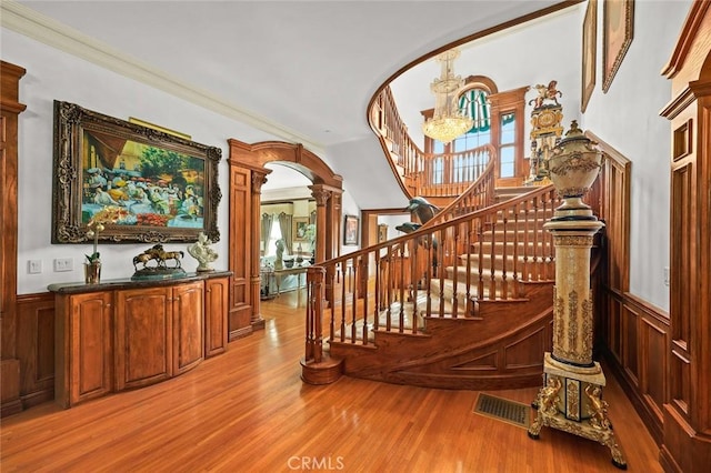 stairway featuring decorative columns, crown molding, wood-type flooring, and a notable chandelier