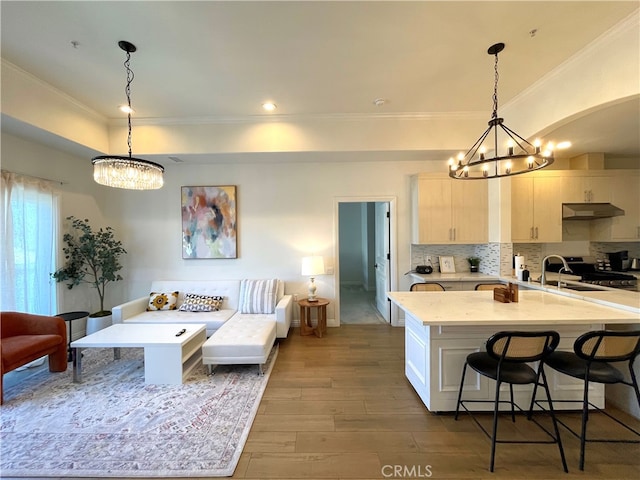 kitchen with light stone counters, light brown cabinetry, dark wood-type flooring, crown molding, and decorative light fixtures