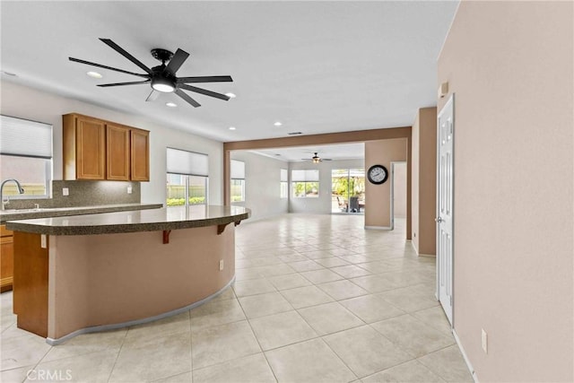 kitchen with dark countertops, brown cabinetry, open floor plan, a sink, and a kitchen bar