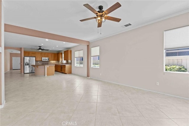 unfurnished living room with a healthy amount of sunlight, ceiling fan, visible vents, and arched walkways