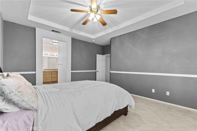 bedroom with a tray ceiling, visible vents, a ceiling fan, ensuite bath, and baseboards