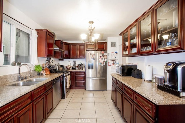 kitchen featuring glass insert cabinets, decorative light fixtures, light stone countertops, stainless steel appliances, and a sink